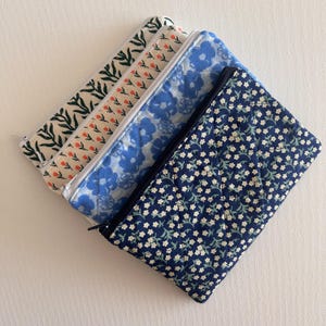 May include: Four quilted fabric pouches with zip closures. The pouches feature floral and botanical patterns in shades of blue, white, and green. The pouches are rectangular and appear to be handmade.