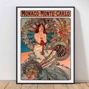 May include: Art Nouveau style poster print of Monaco-Monte-Carlo. The artwork features a woman with red hair and a white dress, surrounded by floral and decorative elements. The poster is framed in black and set against a white wall.