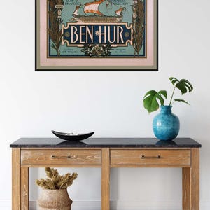 K&ouml;nnte beinhalten: Ein gerahmtes Vintage-Poster f&uuml;r die Illinois Theatre-Produktion von "Ben-Hur". Das Poster zeigt ein Schiff mit orangefarbenen Segeln vor hellblauem Hintergrund, mit Text in dekorativer Schrift. Das Poster h&auml;ngt &uuml;ber einer Holzkonsolentisch.