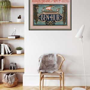 K&ouml;nnte beinhalten: Ein gerahmtes Vintage-Poster f&uuml;r das Theaterst&uuml;ck "Ben Hur" h&auml;ngt an einer wei&szlig;en Wand. Das Poster zeigt eine Schiffsillustration mit dem Text "Illinois Theatre Chicago" und "Sept 2". Unter dem Poster steht ein Holzstuhl mit einem grauen Fell.