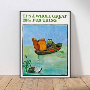 May include: Framed print with a cartoon frog in a boat, reading a book. The frog is wearing a green bow tie and jacket. The text at the top reads "IT'S A WHOLE GREAT BIG FUN THING". The artwork is set against a blue sky and water background.