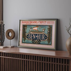 K&ouml;nnte beinhalten: Gerahmtes Vintage-Theaterplakat f&uuml;r "Ben Hur" im Illinois Theatre in Chicago. Das Plakat zeigt eine Schiffsillustration mit roten Segeln und dem Text "Ben Hur" in einer dekorativen Schriftart. Das Plakat ist in einem silbernen Rahmen gerahmt.