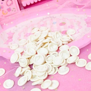 May include: A large pile of white finger cots on a pink and white background. The finger cots are made of a thin, flexible material and are designed to protect fingers from dirt and grime.