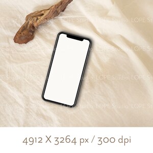 Pu&ograve; includere: Uno smartphone nero con uno schermo bianco &egrave; sdraiato su una superficie di tessuto beige. Un pezzo di legno alla deriva si trova nell'angolo in alto a sinistra dell'immagine.