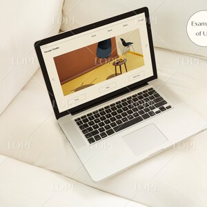 Puede incluir: Un port&aacute;til plateado que muestra un sitio web con el texto "Voyage Studio" en un sof&aacute; blanco. El sitio web muestra elementos de dise&ntilde;o de interiores. Un peque&ntilde;o c&iacute;rculo blanco con el texto "Examples of Use" est&aacute; en la esquina superior derecha.