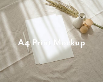 Puede incluir: Una hoja de papel blanca A4 sobre una superficie de tela beige con un bolígrafo blanco y un pequeño jarrón con flores secas. El texto "A4 Print Mockup" está impreso en el papel.