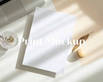 Puede incluir: Una hoja de papel blanca sobre una superficie blanca con una bola de madera y una hoja seca sobre una superficie beige. El texto "Print Mockup" está impreso en el papel.