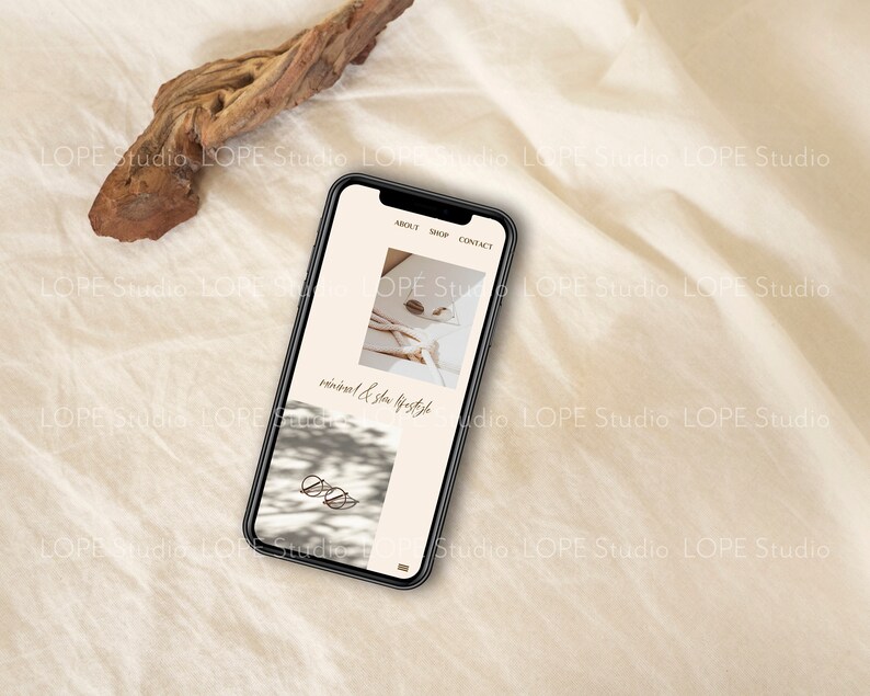 Pu&ograve; includere: Uno smartphone che mostra un sito web con il testo "minimal & slow lifestyle" e immagini di un letto bianco con un libro e un paio di occhiali su una superficie bianca.