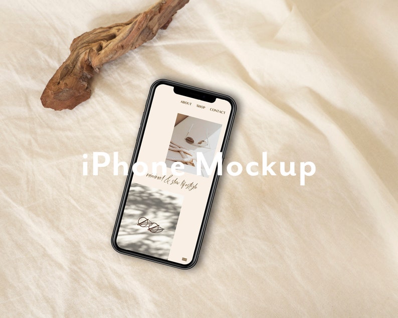 Pu&ograve; includere: Un mockup di iPhone nero su uno sfondo di lino bianco con un pezzo di legno alla deriva. Lo schermo del telefono mostra un sito web con il testo "minimal & slow lifestyle" e le parole "About, Shop, Contact".