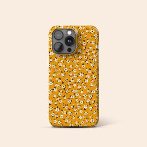 May include: A yellow phone case with a white floral pattern.