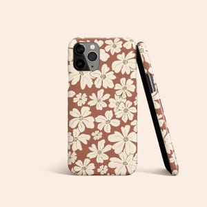 May include: A brown phone case with a white floral pattern. The case has a camera cutout and a black side.