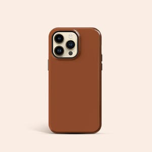 Puede incluir: Una funda de teléfono de cuero marrón para un iPhone con una protuberancia de cámara.