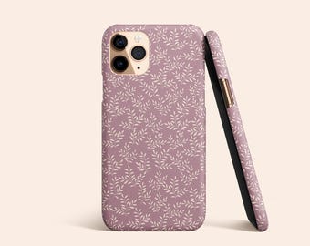 Può includere: Una custodia per telefono malva con un motivo floreale bianco. La custodia ha un rialzo per la fotocamera e un accento dorato sul lato.