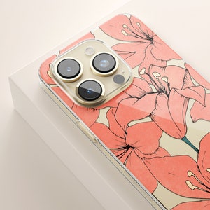 Puede incluir: Una funda transparente para tel&eacute;fono con un dise&ntilde;o floral. La funda tiene un patr&oacute;n floral rosa y blanco con una cubierta de lente de c&aacute;mara dorada.