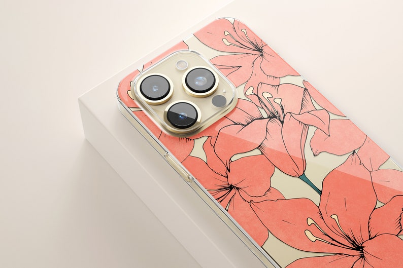 Puede incluir: Una funda transparente para tel&eacute;fono con un dise&ntilde;o floral. La funda tiene un patr&oacute;n floral rosa y blanco con una cubierta de lente de c&aacute;mara dorada.