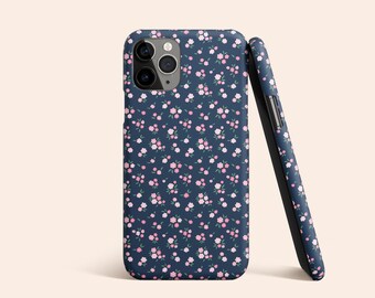 Può includere: Una custodia per telefono blu scuro con un motivo floreale rosa e bianco. La custodia ha un ritaglio per l'obiettivo della fotocamera.