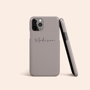 Puede incluir: Funda de teléfono gris claro con el nombre "Madison" en escritura cursiva. La funda está apoyada contra otra, revelando un interior negro. La funda del teléfono tiene un módulo de cámara con tres lentes.