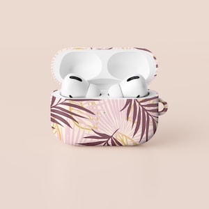 Könnte beinhalten: Eine rosa und weiße Airpods-Hülle mit einem tropischen Blatt-Muster. Die Hülle ist geöffnet und die weißen Airpods sind im Inneren sichtbar.