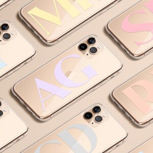 Puede incluir: Una colección de fundas de iPhone doradas con letras de diferentes colores en la parte posterior. Las letras son "AG", "CD", "JN", "MI", "RE" y "SB".
