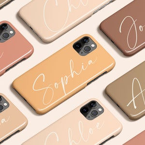 Puede incluir: Una colección de fundas para teléfonos con diferentes nombres escritos en letra cursiva. Las fundas son de varios tonos de marrón, beige y melocotón.