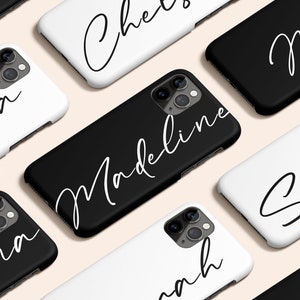 Puede incluir: Una colección de fundas de teléfono personalizadas con nombres escritos en cursiva. Las fundas son negras y blancas y presentan una variedad de nombres, incluyendo Kayla, Madeline, Sophia, Mia y Anna.