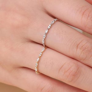 May include: Two delicate rings, one gold and one silver, each adorned with small, sparkling stones, are displayed on a hand. The rings are thin and elegant, suggesting a minimalist jewelry style. The background includes a teacup and a neutral-toned surface.