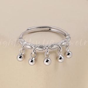 Könnte beinhalten: Ein verstellbarer Silberring mit filigranem Design. Der Ring hat eine Reihe kleiner, hängender silberner Kugeln, die am Band befestigt sind. Der Ring wird vor einem neutralen Hintergrund präsentiert. Der Text "Lights You Up Jewelry" ist sichtbar.