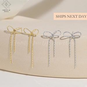 Puede incluir: Dos pares de pendientes colgantes con un diseño de lazo. Un par es dorado y el otro es plateado.