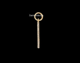 Puede incluir: Un dije de oro con una barra larga, delgada e incrustada de diamantes que cuelga de un bucle circular.