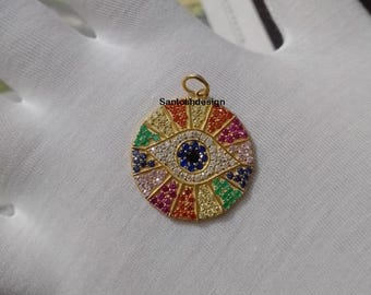 May include: A gold pendant featuring a round, colourful evil eye design. The eye is encircled by a circle of small, colourful gemstones. The pendant is displayed against a white background.