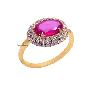 May include: A gold ring with a large oval-shaped ruby surrounded by a halo of smaller diamonds.