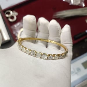 Op de afbeelding: Een gouden armband met een rij ronde, witte, bezel-gezet diamanten. De armband ligt op een wit oppervlak.