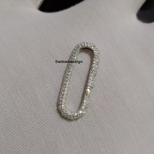 May include: A silver oval-shaped charm with a pave setting of small clear stones. The charm is designed to be used as a connector for jewelry.