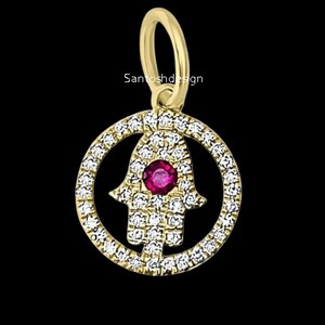 May include: A gold charm with a hamsa hand design, set with small clear stones and a single red stone in the center. The charm is attached to a gold loop.