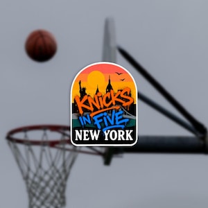 Op de afbeelding: Een sticker met een silhouet van de skyline van New York bij zonsondergang met de tekst KNICKS IN FIVE in oranje en blauwe graffitiletters, en de woorden NEW YORK in witte blokletters onderaan, geplaatst voor een basketbalring.