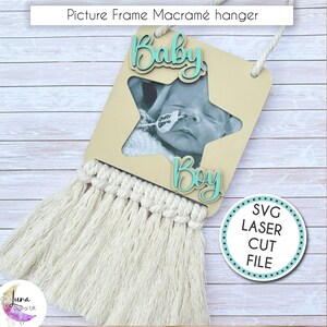 Puede incluir: Un colgador de macramé para marco de fotos beige con una abertura para fotos en forma de estrella. Las palabras "Baby" y "Boy" están en escritura turquesa. La parte inferior presenta una franja de macramé color crema. El texto "SVG Laser Cut File" está en un círculo.