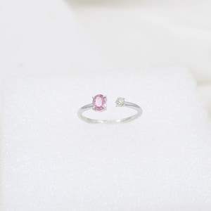 May include: Open-style ring with a silver band. The ring features a pink oval-cut gemstone and a smaller, round, clear gemstone. The ring is set against a white background.