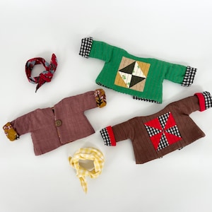 Peut inclure: Trois vestes de poupée faites à la main avec différents motifs de patchwork. Une veste est verte avec un motif noir et blanc, une autre est marron avec un motif rouge et blanc et la dernière est rose avec un motif jaune et marron. Les vestes sont toutes faites dans un tissu doux et matelassé.