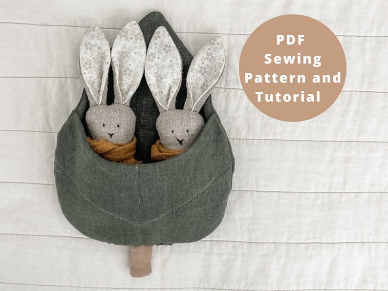 May include: A PDF sewing pattern and tutorial for making a plush leaf-shaped pillow with two bunny rabbits inside. The pillow is made of a dark green fabric and the bunnies are made of a light brown fabric with white ears.