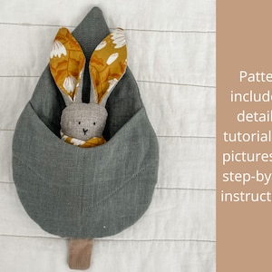 May include: A gray fabric leaf-shaped pouch with a bunny rabbit toy inside. The bunny has yellow and white floral fabric ears and a gray fabric body.