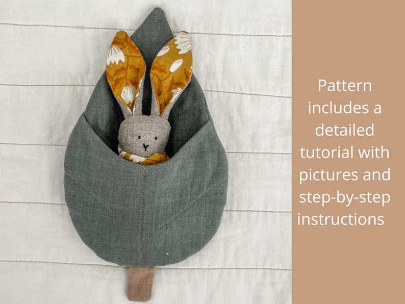 May include: A gray fabric leaf-shaped pouch with a bunny rabbit toy inside. The bunny has yellow and white floral fabric ears and a gray fabric body.