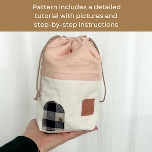 May include: A pink and white drawstring bag with a black and white checkered fabric patch and a brown fabric patch. The bag is made of linen and has a simple design.