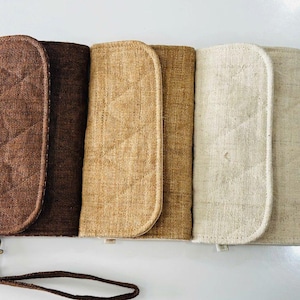 May include: A collection of four fabric wristlet wallets in shades of brown and beige. The wallets have a quilted pattern and a wrist strap with a metal clasp. The wallets are made of a textured fabric.