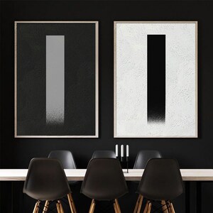 May include: Two framed abstract art prints with black and white vertical lines. The print on the left has a gray line on a black background. The print on the right has a black line on a white background.