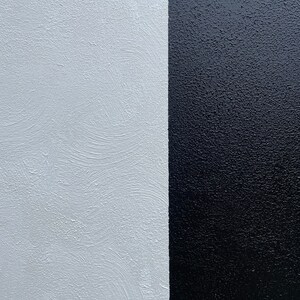 May include: A close-up of a wall painted half white and half black. The white side has a textured finish, while the black side is smooth.