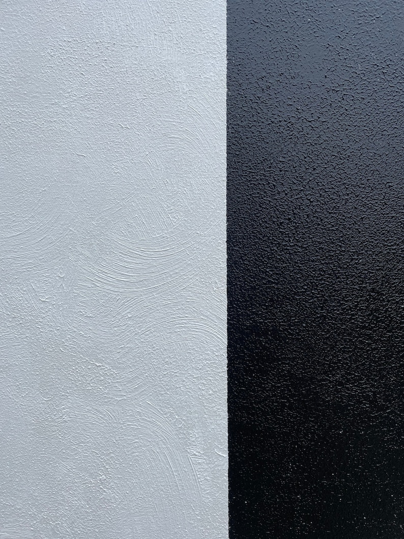May include: A close-up of a wall painted half white and half black. The white side has a textured finish, while the black side is smooth.