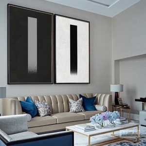 May include: Two abstract paintings with a black and white color scheme. The paintings are framed and hung on a wall in a living room setting.