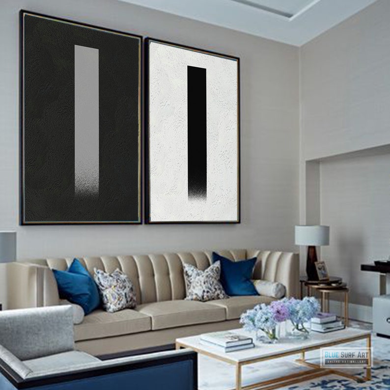 May include: Two abstract paintings with a black and white color scheme. The paintings are framed and hung on a wall in a living room setting.