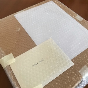 May include: A brown cardboard box wrapped in bubble wrap with a white envelope on top. The envelope has the words "Thank You!" written on it.