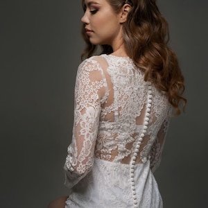 以下が含まれることがあります： 長袖でボタン留めのバックスタイルの白いレースのボディスーツです。